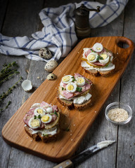Sandwiches on cereal bread with cheese, meat, and quail eggs on a wooden board.