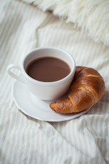 A cup of hot cocoa, a croissant on the bed. Cozy. Homeliness.