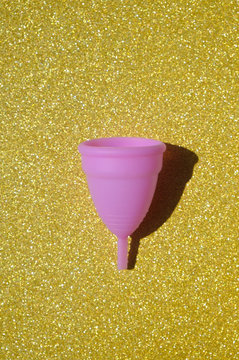 Pink menstrual cup on gold shiny background