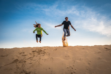 Caucasian girl and man jumping over the top of a big sand dune