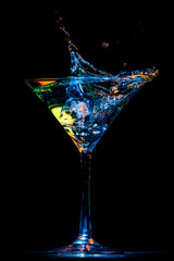 Copa de martini con líquido salpicando en tonos verde y azul, vertical sobre fondo negro