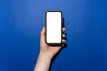 Close-up of male hand holding smartphone in case with mockup on background of phantom blue color.