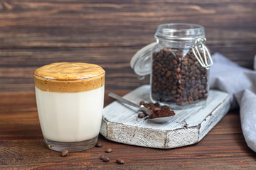 Dalgona coffee is a trendy cold Korean drink. Tasty, aromatic coffee with milk and sugar in a glass on a wooden background.