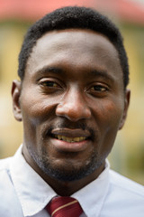 Face of happy young handsome African businessman smiling outdoors