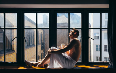 Adult man enjoying the sun rays sitting besides the window in the morning