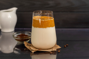 Dalgona coffee is a trendy cold Korean drink. Tasty, aromatic coffee with milk and sugar in a glass on a black background. Copy space