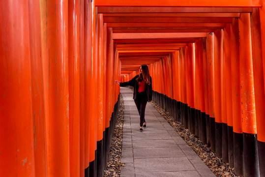 Woman walking under orange wooden pillars, Kyoto, Japan