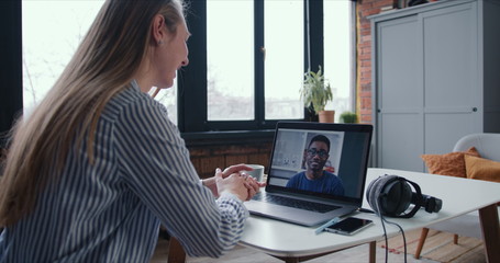 Happy young Caucasian tutor woman chatting with African male friend at home using laptop video conference call online.