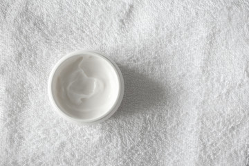 Moisturizer cream or body lotion on white bathroom towel background and copy space. Daily skincare routine, top view