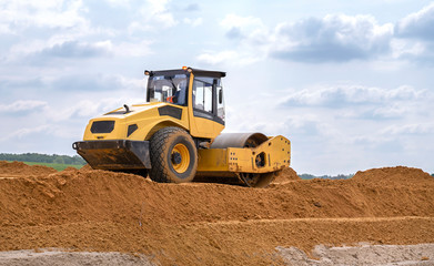 Construction machinery paver stands on a pile of sand against a blue sky