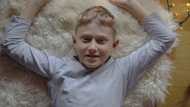 4K close up portrait footage of boy lying on sheep skin rug Christmas lights around