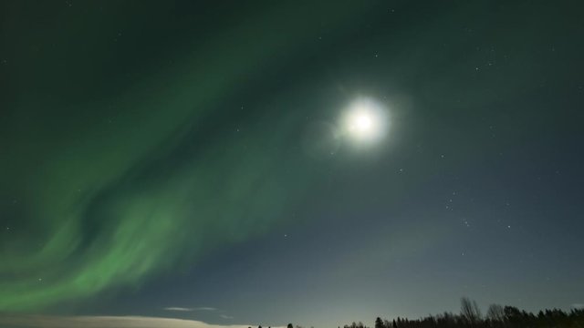 Video of brilliant green Aurora shining over Swedish frozen lake and winter landscape, light rays from a full moon in different soft colors, moving camera close up view, Northern Sweden, Lapland