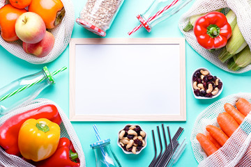 White board for meal plan or diet strategy with fresh vegetables and fruits in mesh bags on blue table top. Zero waste accessories, leading healthy and sustainable lifestyle, top view