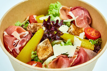 Salad with jamon, parmesan and feta cheese, cherry tomatoes, pear, lettuce, sun-dried tomatoes in a cardboard box