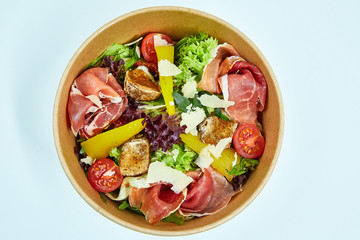 Salad with jamon, parmesan and feta cheese, cherry tomatoes, pear, lettuce, sun-dried tomatoes in a cardboard box