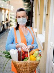Portrait of a volunteer girl in a protective mask and medical gloves near the house of a man who is on self-isolation