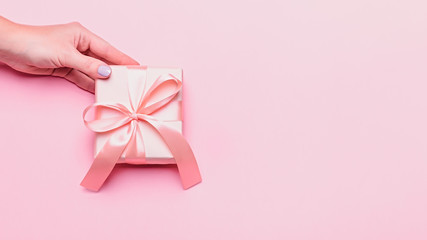 Woman holding pink gift box on pastel background, copyspace. Mother's Day or Women's Day card in trendy colors, top view