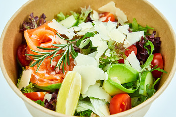 Salad with salmon and cherry tomatoes, lemon, avocado, cucumber, lettuce, arugula, Parmesan cheese, a sprig of rosemary in a cardboard box