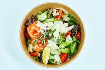 Salad with salmon and cherry tomatoes, lemon, avocado, cucumber, lettuce, arugula, Parmesan cheese, a sprig of rosemary in a cardboard box