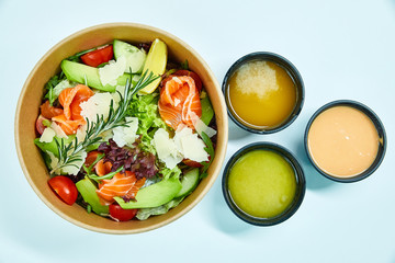 Salad with salmon and cherry tomatoes, lemon, avocado, cucumber, lettuce, arugula, Parmesan cheese, a sprig of rosemary in a cardboard box