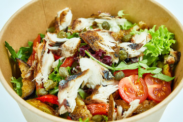 Sea fish salad with cherry tomatoes, capers, grilled vegetables, lettuce in a cardboard box