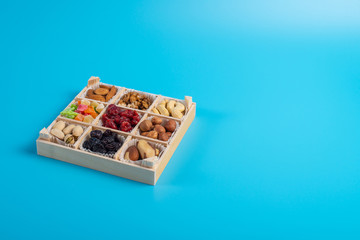 Assorted dried fruits and nuts in a wooden box isolated on a blue background. Raisins, candied fruits, cherries, Brazil nuts, hazelnuts, walnuts, almonds, cashews, pistachios.