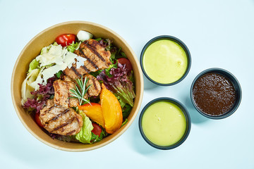 Salad with grilled pork, parmesan cheese, cherry tomatoes, lettuce, arugula, quail eggs, persimmon, a sprig of rosemary in a cardboard box