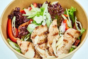 Salad with grilled chicken, parmesan cheese, cherry tomatoes, sun-dried tomatoes, lettuce, red pepper, celery in a cardboard box