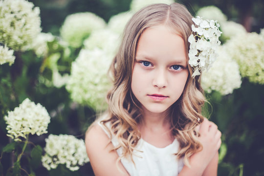 Fashion close-up portrait of beautiful 9 -10 years old girl posing against blooming white hydrangea flowers.