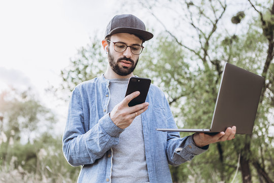 Freelancer working outdoors with laptop. young man with laptop in park across green nature on a sunny day. Freelance concept