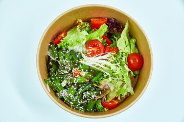 Vegetable salad with cherry tomatoes, cucumber, lettuce, arugula, asparagus beans and sesame seeds in a cardboard box