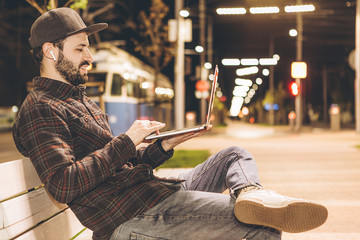 attractive young businessman working on startup sitting with laptop on the street. Freelance work concept.