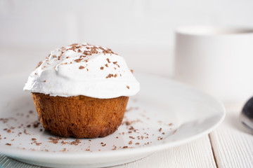 Cupcakes with whipped cream and chocolate chips on a white plate and a Cup of coffee in the background, on a white wooden table. Image for the menu or catalog of confectionery products.