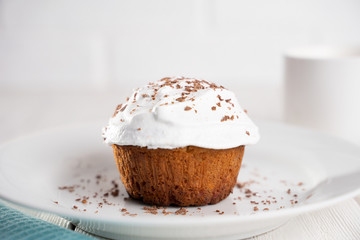 Cupcakes with whipped cream and chocolate chips on a white plate and a Cup of coffee in the background, on a white wooden table. Image for the menu or catalog of confectionery products.