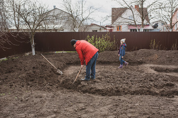 A man with children digs the ground with a shovel in the spring. Do-it-yourself pond