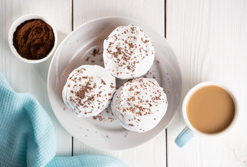 Cupcakes with whipped cream and chocolate chips on a white plate and a Cup of coffee in the background, on a white wooden table. Image for the menu or catalog of confectionery products.