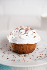 Cupcakes with whipped cream and chocolate chips on a white plate and a Cup of coffee in the background, on a white wooden table. Image for the menu or catalog of confectionery products.