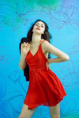 Dark-haired female model posing in red dress on flower background