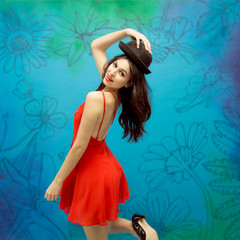 Dark-haired female model with hat posing in red dress on flower background