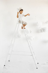 portrait of a cute little boy in crown on white ladder among clouds on a white background