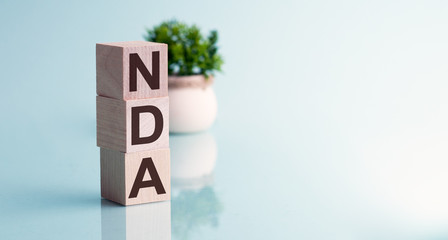 NDA-text on wooden cubes, on a blue background. In the background, a green plant in a white pot. Reflection in a mirror surface