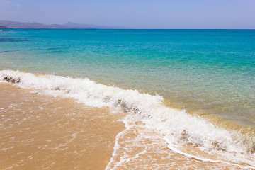Small wave splashing on seashore with vast turquoise water sea on background. Paradise destination with empty beach in Fuerteventura island, Spain. Summer vacation, travel concepts
