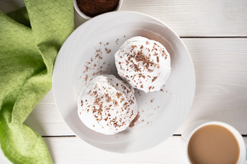 Fototapeta na wymiar Cupcakes with whipped cream and chocolate chips on a white plate and a Cup of coffee in the background, on a white wooden table. Image for the menu or catalog of confectionery products.