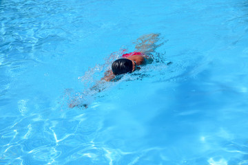 Caucasian man swims in freestyle (crawl) at the outdoor swimming pool on a sunny summer day