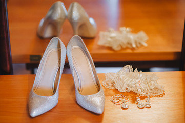 Accessories of the bride against the background of a mirror with reflection: shoes, garter, earrings, pendant. Photography, concept.