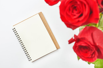 Top view shot of empty blank notebook diary and red roses on white table