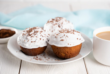 Cupcakes with whipped cream and chocolate chips on a white plate and a Cup of coffee in the background, on a white wooden table. Image for the menu or catalog of confectionery products.