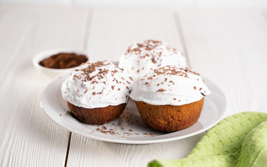 Cupcakes with whipped cream and chocolate chips on a white plate and a Cup of coffee in the background, on a white wooden table. Image for the menu or catalog of confectionery products.