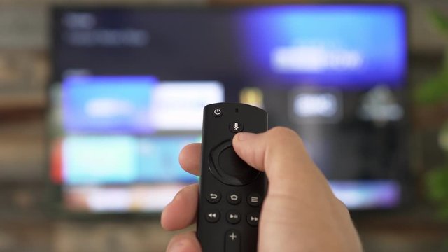 Male hand holding the TV remote control and changing TV channels