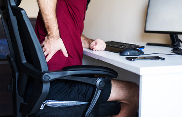 Man having back pain while working from home in an improvised office